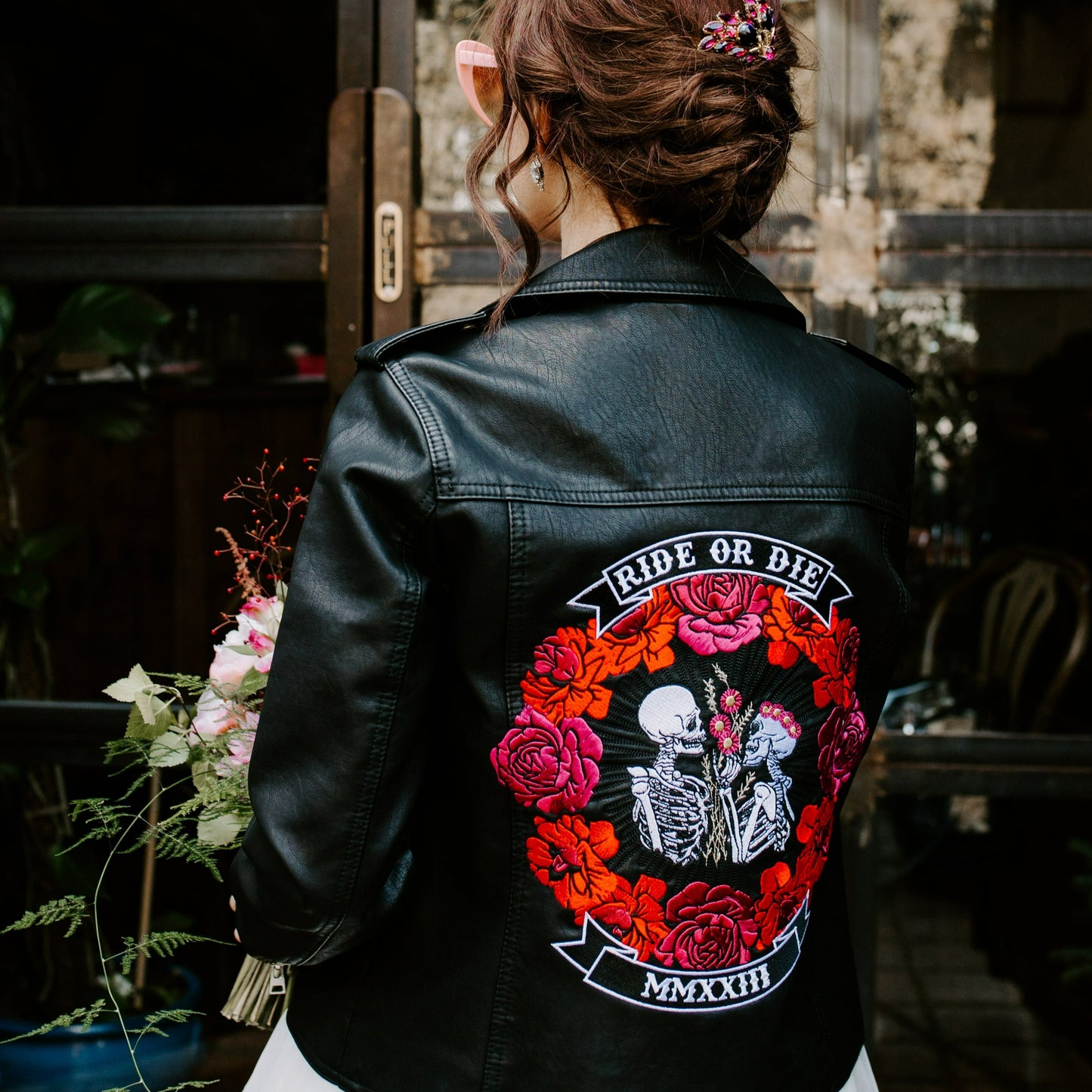 Black leather bridal jacket featuring a Ride Or Die Floral Skeleton Couple – a chic and unconventional cover-up for the modern bride